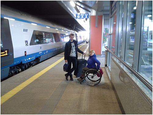 Autorka na wózku z asystentem na peronie, w tle pociąg Pendolino