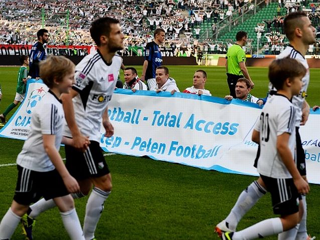 Piłkarze wchodzą na murawę, w tle baner akcji CAFE "Pełen dostęp, Pełen football"