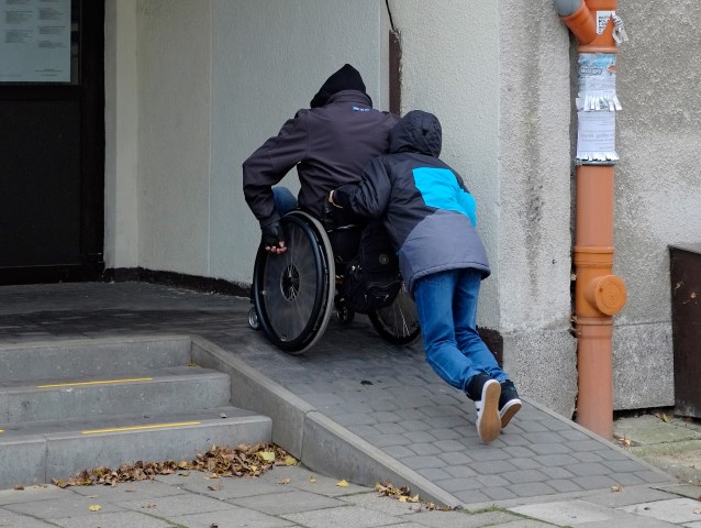 po podjeździe wjeżdża wózkowicz popychany przez chłopca