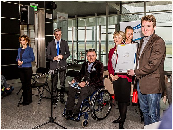 Siedzący na wózku Bartłomiej Skrzyński wraz z przedstawicielami lotniska prezentują przyznany certyfikat