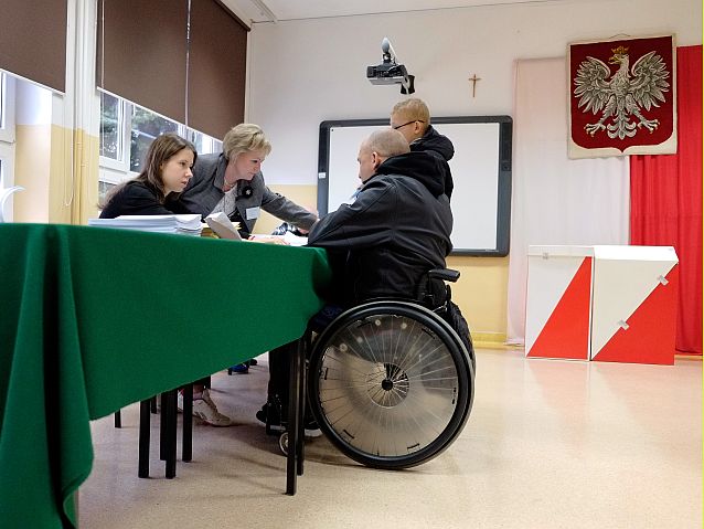 Mężczyzna na wózku przy stoliku komisji wyborczej w lokalu wyborczym