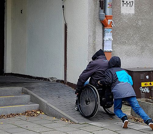 Chłopiec pcha wózek z mężczyzną po pochylni