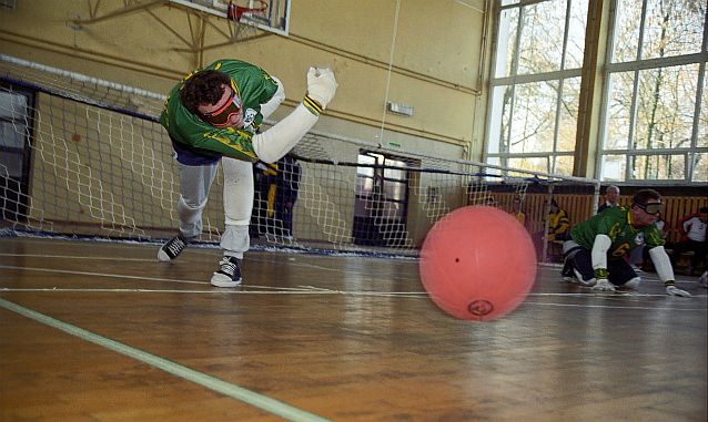 Mężczyzna stojąc rozpędza piłkę, by turlała się po boisku