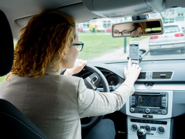 kobieta prowadzi samochód, wpisując adres do nawigacji telefonu