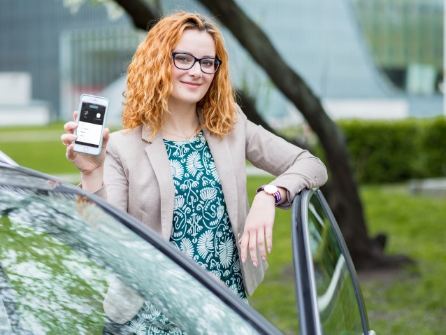 Iwona Cichosz stoi przy samochodzie pokazując telefon