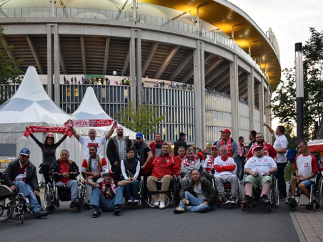 kilkunastu kibiców dwóch płci pozuje do zdjęciu pod stadionem we Frankfurcie