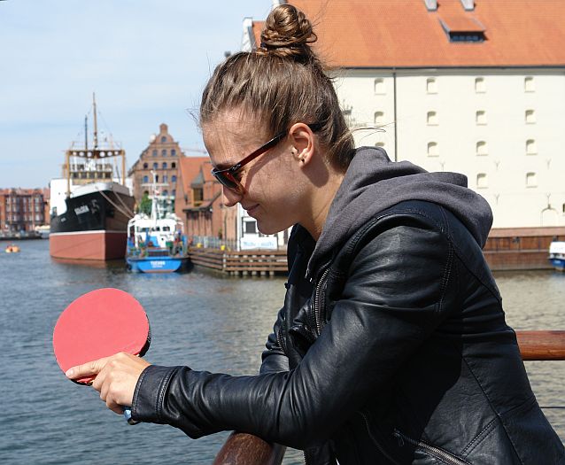 Natalia Partyka stoi na nabrzeżu rzeki i patrzy na swoją rakietkę do tenisa stołowego