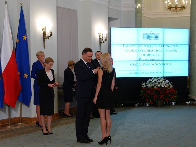 Reprezentacyjna sala w Pałacu Prezydenckim. Prezydent na środku przypina odznaczenie do sukienki Barbarze Niewiedział