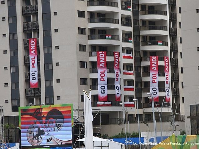 Wieżowce wioski olimpijskiej z flagami biało-czerwonymi i napisem Go Poland