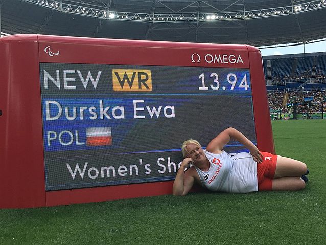 Ewa Durska leży przed tablicą ze swoim nazwiskiem i wynikiem nowego rekordu świata (13,94 m)
