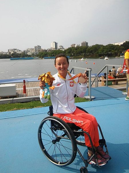 Uśmiechnięta Kamila Kubas siedzi na wózku, trzyma w ręku brązowy medal
