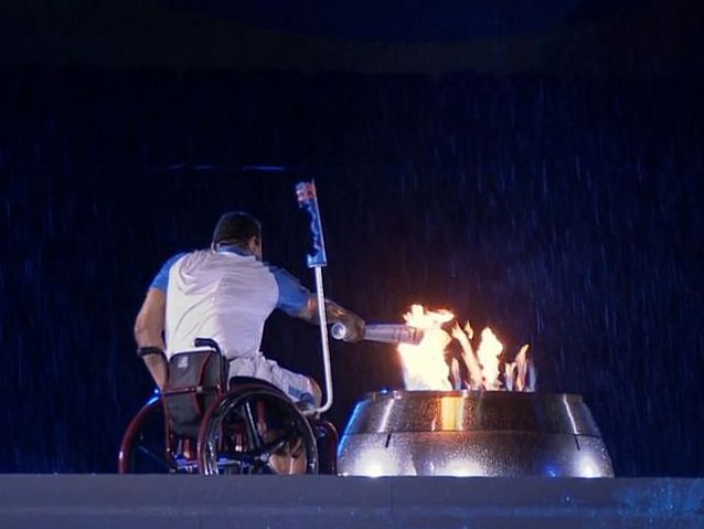 Mężczyzna na wózku zapala znicz paraolimpijski