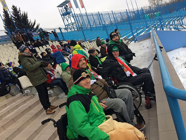 Siedzący na wózkach kibice Śląska Wrocław na trybunach niewielkiego stadionu zimą