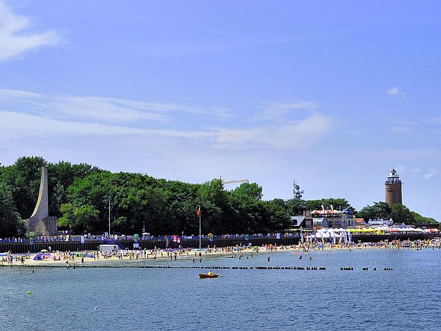 Widok od strony morza na plażę w Kołobrzegu. Po lewej pomnik, po prawej latarnia morska