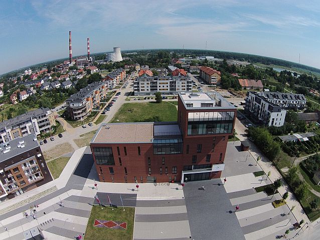 Widok z lotu ptaka na nowoczesny budynek i plac wokół niego, w tle panorama miasta z elektrownią