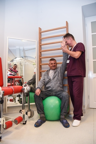 rehabilitant pomaga w rehabilitacji pacjenta w średnim wieku, unosi jego rękę