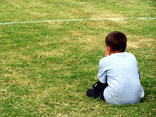 chłopiec siedzi sam na boisku