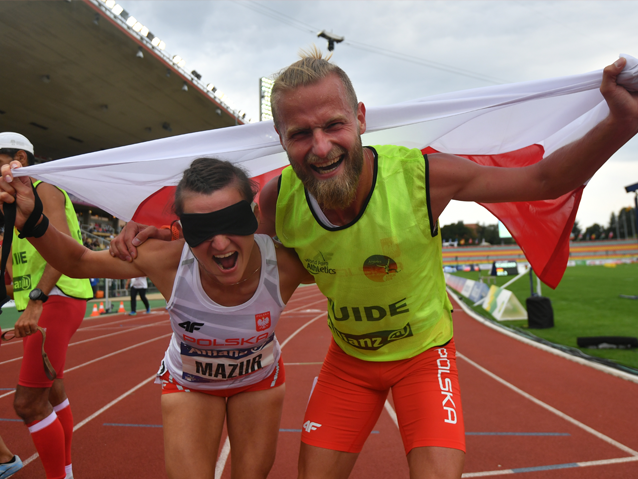 Joanna Mazur i Michał Stawicki krzyczą ze szczęścia po biegu, razem trzymając flagę
