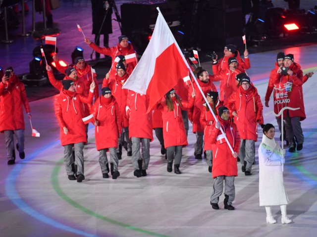 Reprezentacja Polski idzie za tabliczką Poland i polską flagą, trzymaną przez Kamila Rosiaka