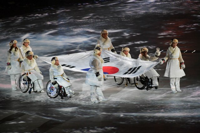 Dziewięciu Koreańczyków w tym czterech na wózkach niosą ogromną flagę Korei Południowej przez stadion