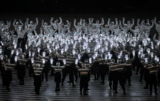 Taniec Koreańczyków w białych strojach z jaśniejącymi rękawicami na dłoniach. Wokół jest dość ciemno
