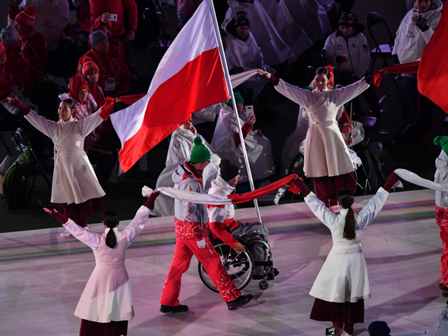 Igor Sikorski porusza się na wózku wraz z przymocowaną do niego flagą. Obok Polaka idzie towarzyszący mu Koreańczyk. 