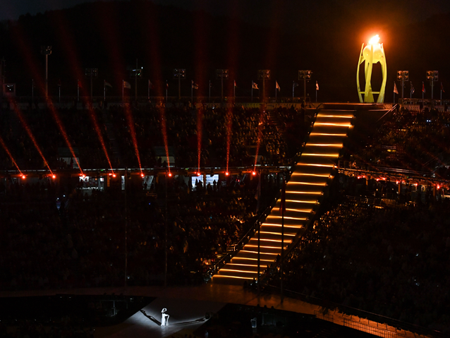 Ostatni taniec przed zgaśnięciem znicza z lotu ptaka. Na scenie z harfą tańczy sama Koreanka, za nią widać wysokie schody, stworzone ze światła i palący się znicz nad stadionem