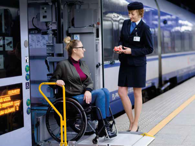kobieta na wózku wysiada z pociągu, obok niej na peronie stoi konduktorka