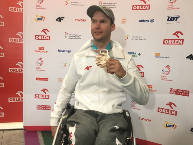 Uśmiechnięty Igor Sikorski siedzi na wózku prezentując brązowy medal