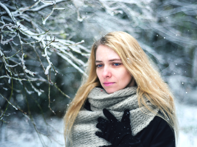 otulona szalikiem kobieta z długimi blond włosami przy ośnieżonych gałęziach