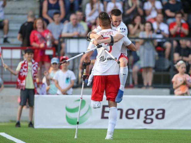 Dwóch zawodnikow ampfutbolu ściska się z radości podczas meczu, w tle kibice na trybunach