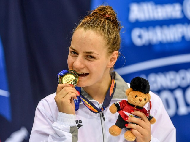Oliwia jabłońska trzyma w zębach medal a w drugiej ręce misia