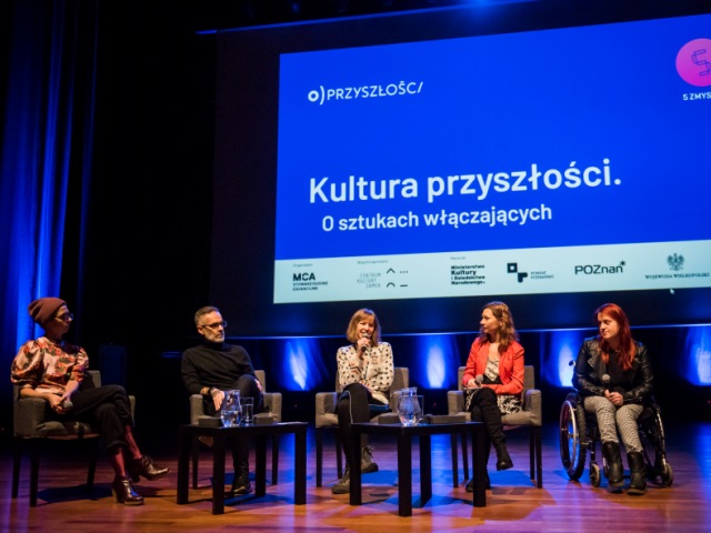 pięc osób w trakcie panelu na scenie ostatnia po prawej kobieta na wózku nad nimi slajd z napisem kultura przyszłości o sztukach włączających