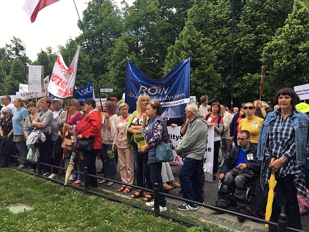 Na jezdni stoją na pierwszym planie kobiety w różnym wieku z transparentami