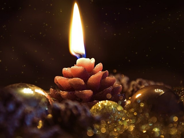 Świąteczny stroik. Bombki i szyszka leżą wokół palącej się świeczki