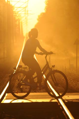 kobieta jedzie na rowerze przez tory kolejowe w słońcu