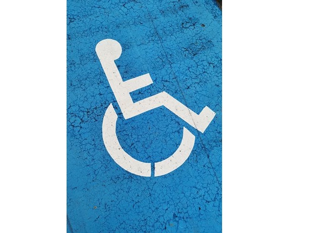 symbol osoby na wózku biały na niebieskim tle, miejsce parkingowe