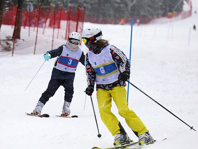 Dwoje narciarzy na stoku, jadący z przodu odwraca głowę, patrząc na tego z tyłu