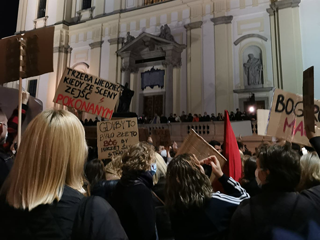 strajkujący przechodzą pod kościołem św. Krzyża w stolicy. Na schodach i rozpiętości kościoła stoi straż narodowa z księdzem