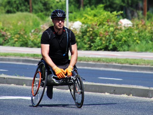 meżczyzna bez nóg na wózku jedzie chodnikiem