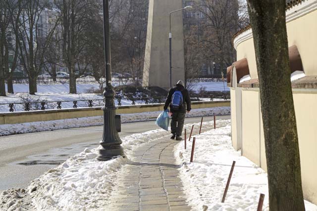 bezdomny mężczyzna z plecakiem i siatką idzie po chodniku