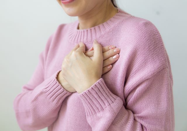 kobieta w różowym swetrze trzyma ręce na sercu