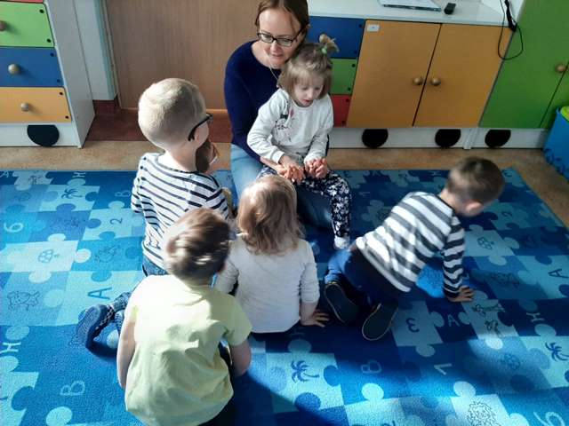 Agnieszka Iwon klęczy na podłodze z dzieckiem na kolanach wokół kilkoro dzieci
