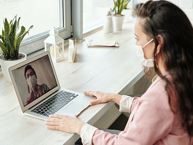 Młoda kobieta rozmawia w maseczce przez laptop z mężczyzną w maseczce