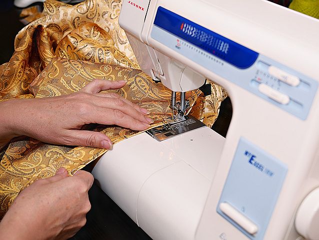 Ręce kobiety zszywającej błyszczący materiał za pomocą maszyny do szycia