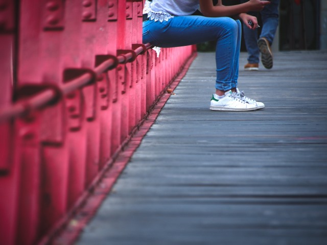 nogi kobiety siedzącej na przęśle mostu w tle oddalające się nogi mężczyzny