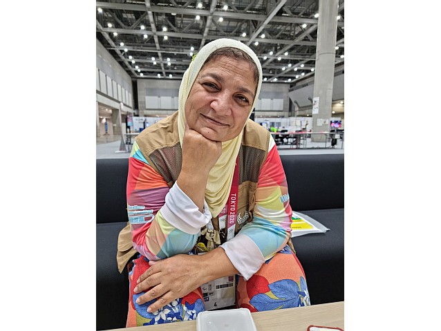 Uśmiechnięta Wadad – kobieta w średnim wieku z chustą na głowie i akredytacją dziennikarską na szyi