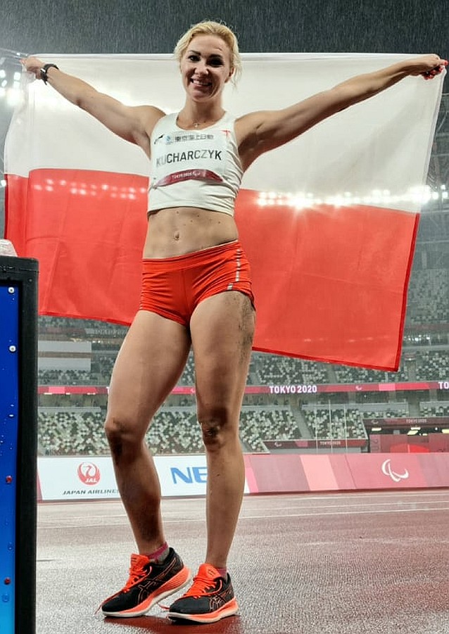 Karolina Kucharczyk stoi na stadionie z rozciągniętą za sobą polską flagą