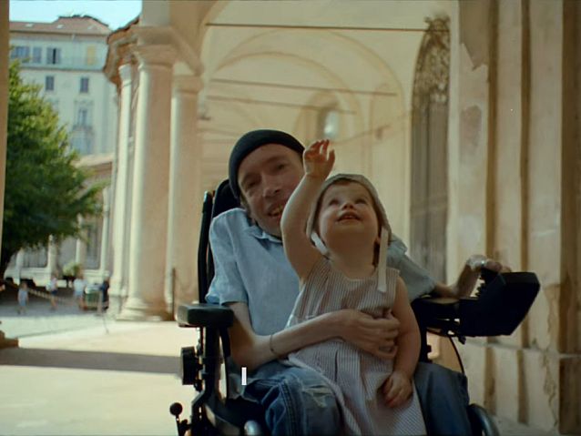 Kadr z filmiku. Młody mężczyzna jedzie elektrycznym wózkiem trzymając na kolanach swoją córeczkę