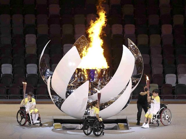 Płyta stadionu w Tokio. Ceremonia otwarcia igrzysk. Trzy osoby na wózkach zapaliły właśnie znicz, który płonie dużym ogniem